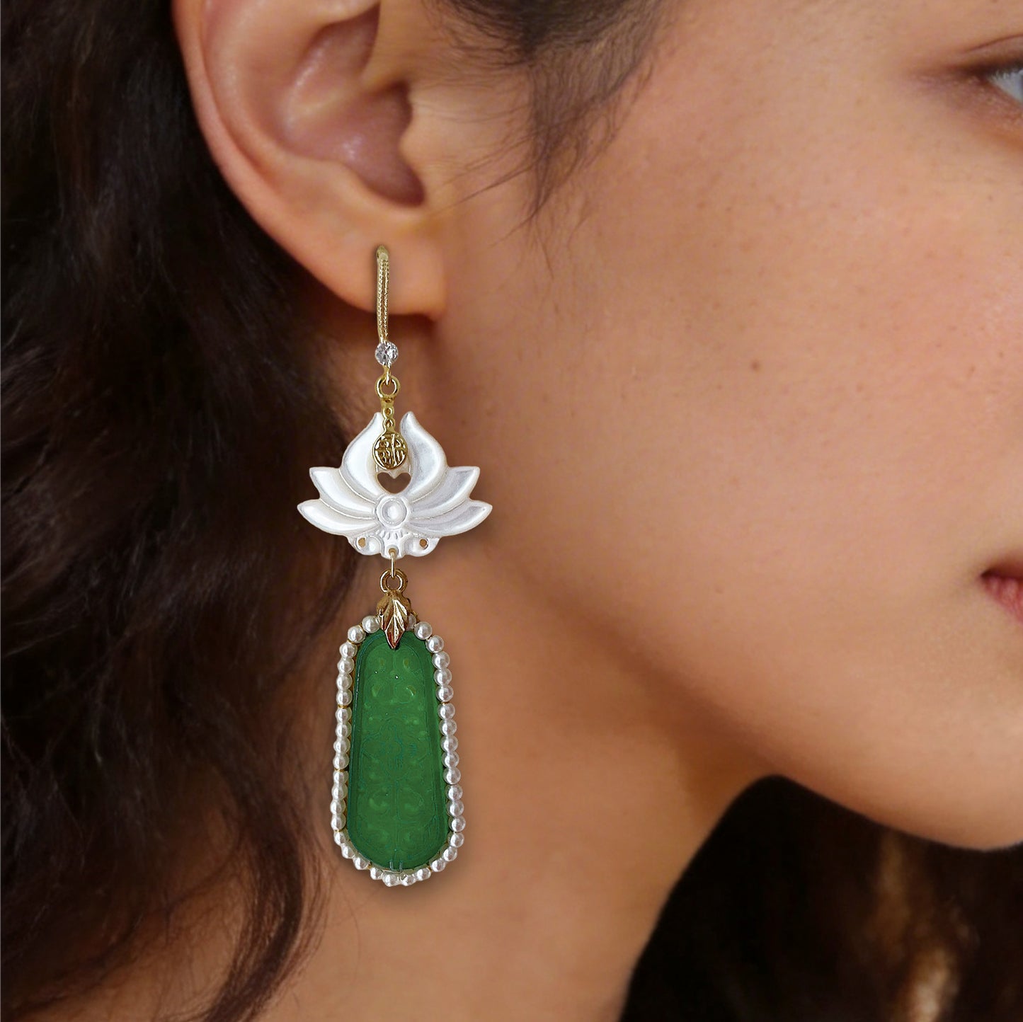 Detailed close up of a delicate carved mother-of-pearl flower and green beaded stone earring worn on the earlobe