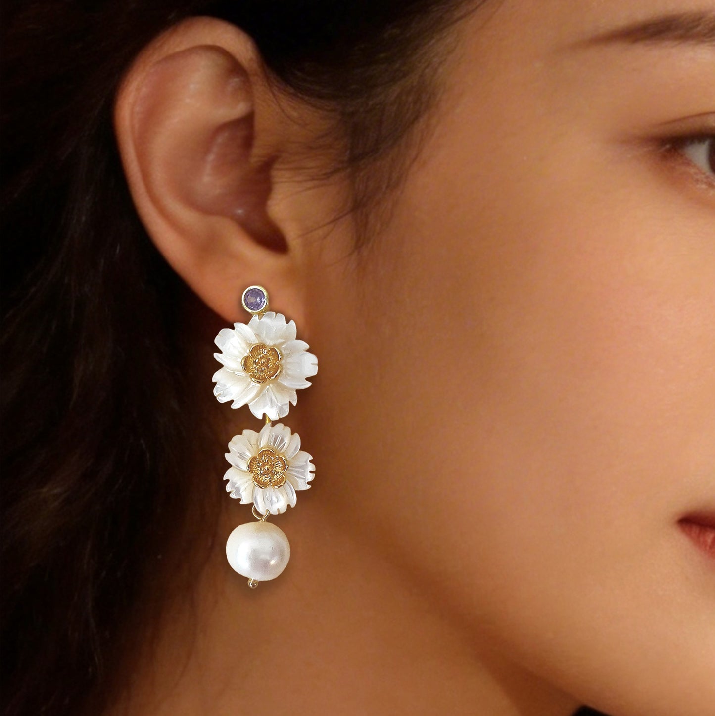 Close up of luminous bloom pearl drop earrings worn on the ear