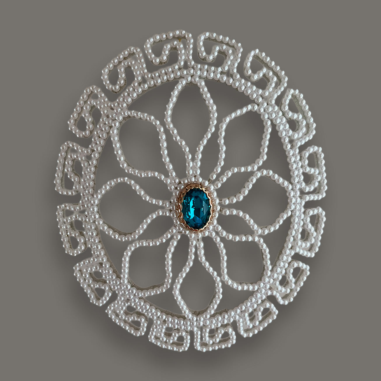 Straight front view of a handcrafted circular pearl bridal hair accessory with intricate geometric pearl patterns and a bright blue central rhinestone, displayed on a neutral grey background.