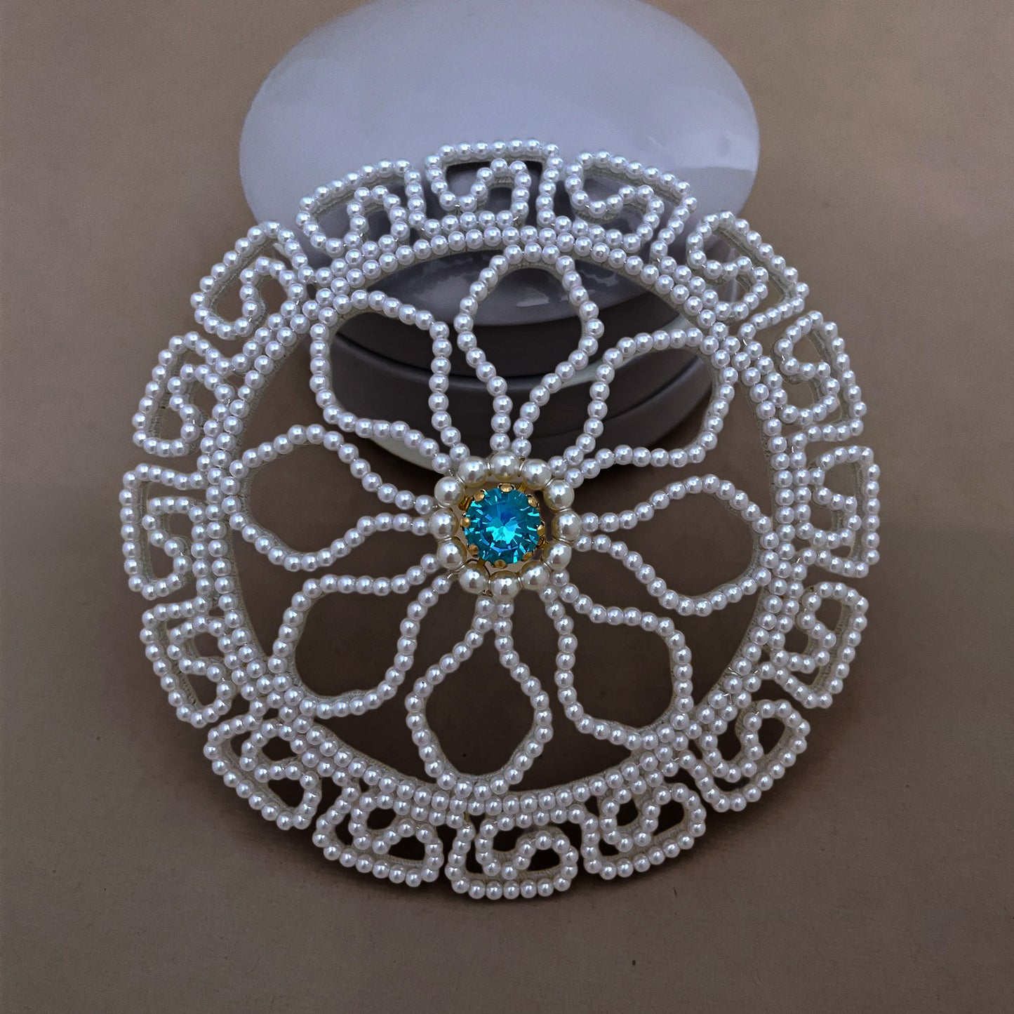 Close-up detail of a handmade pearl chignon cover for weddings, highlighting the lustrous white beads and blue crystal center.