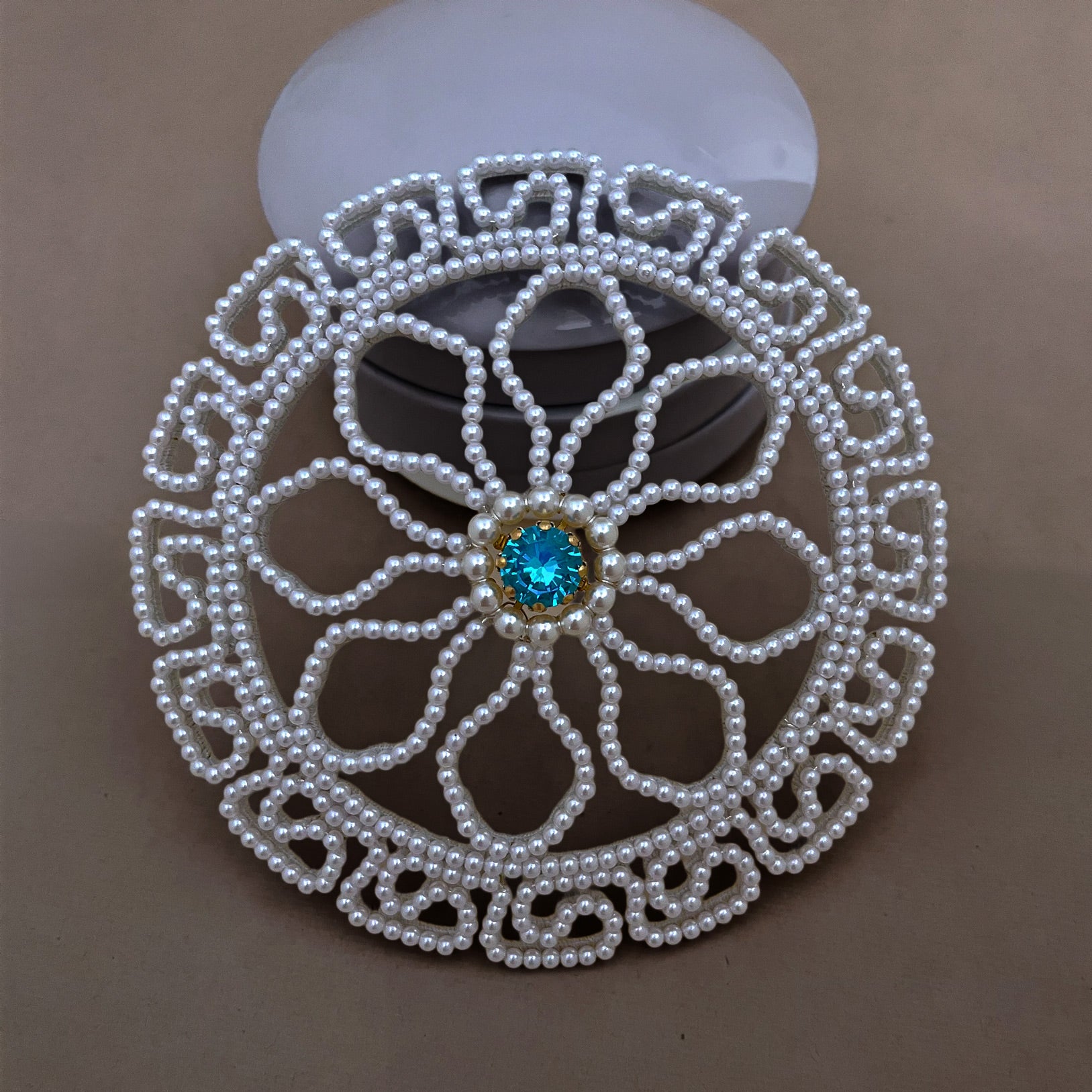 Close-up detail of a handmade pearl chignon cover for weddings, highlighting the lustrous white beads and blue crystal center.