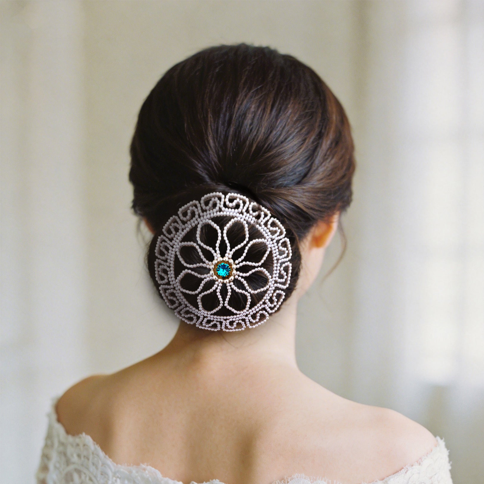 Back view of an elegant bride wearing a pearl hair bun cover over a low chignon hairstyle, showcasing the elegant wedding day look.