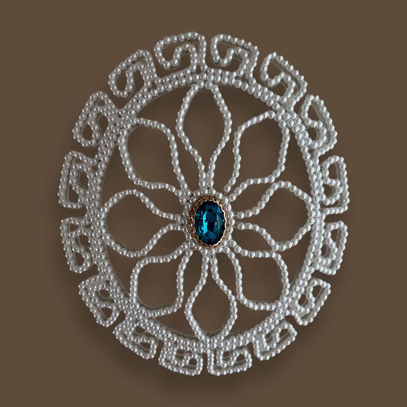 Top-down view of a perfectly symmetrical round pearl wedding hairpiece, showcasing the detailed geometric beadwork and a sparkling blue gemstone center, perfect for a bride's 'something blue'.