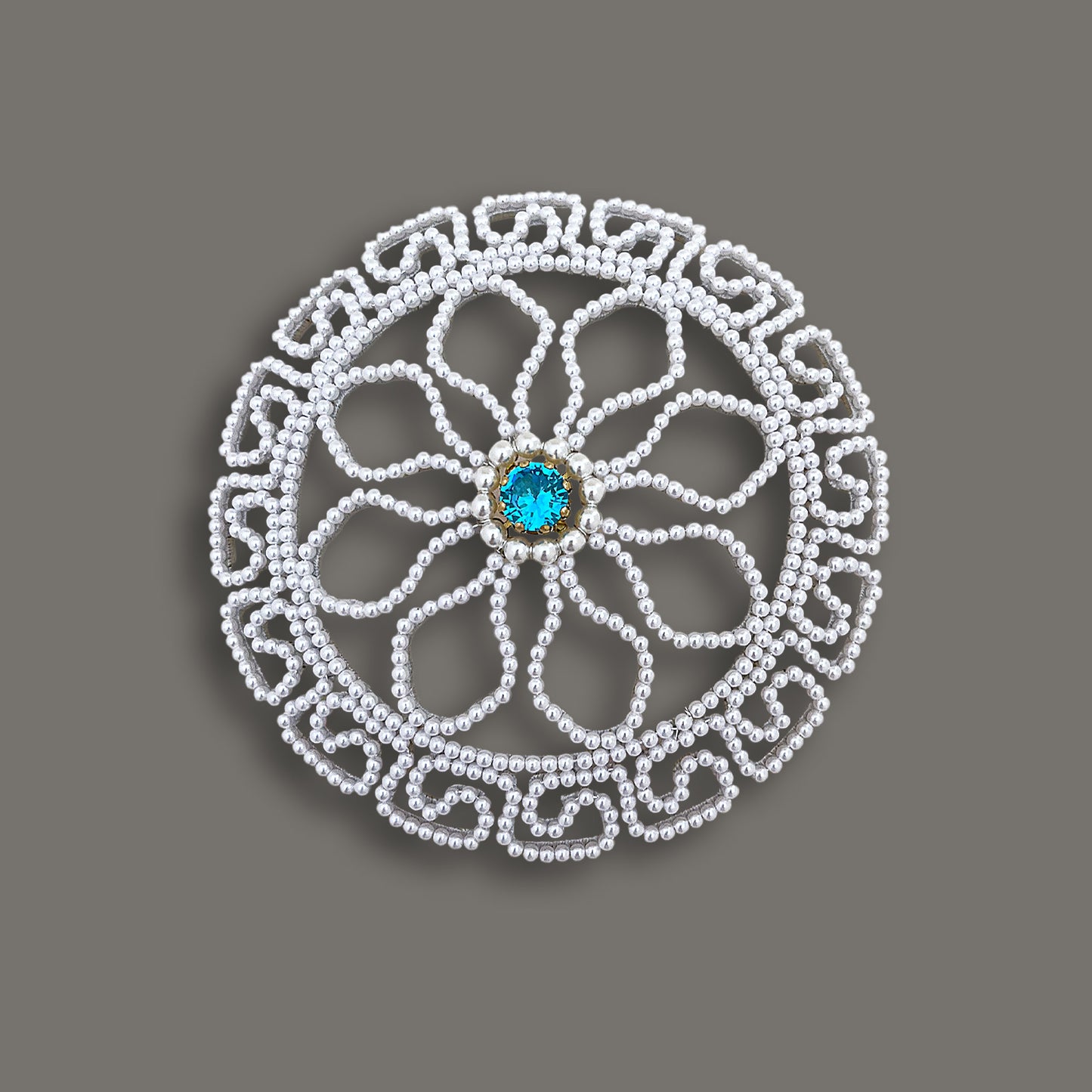 Overhead view of a round vintage pearl bridal bun cover featuring an intricate floral bead pattern and a bright blue central gemstone.