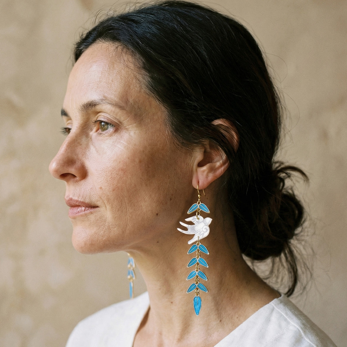 Elegant woman styling mother-of-pearl bird earrings as a stunning something blue for a wedding or special event