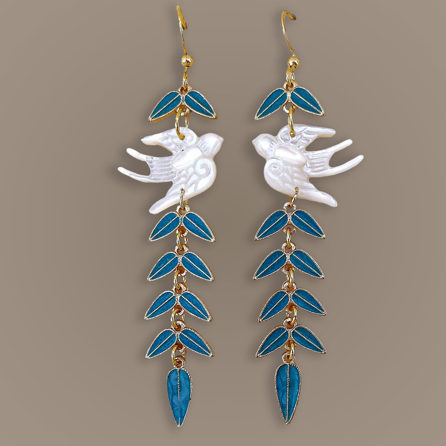 Symmetrical flat lay of carved white bird drop earrings featuring cascading azure blue leaves and gold details