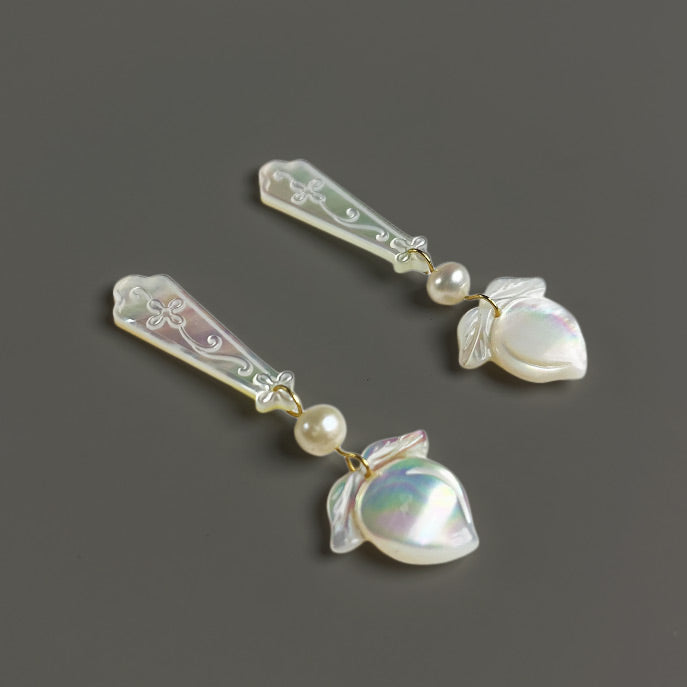Close-up flat lay view of the hand-carved white lip shell flower studs and natural freshwater pearl drops on a warm grey background.