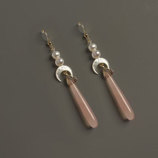 Handcrafted long drop earrings featuring translucent pink agate teardrops, carved mother of pearl crescent moons, and genuine freshwater pearls on a warm grey background.