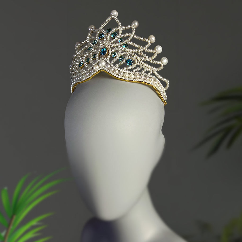Straight front view of the elegant pearl wedding crown on a mannequin, showcasing the symmetrical peak design and sparkling blue centerpieces.