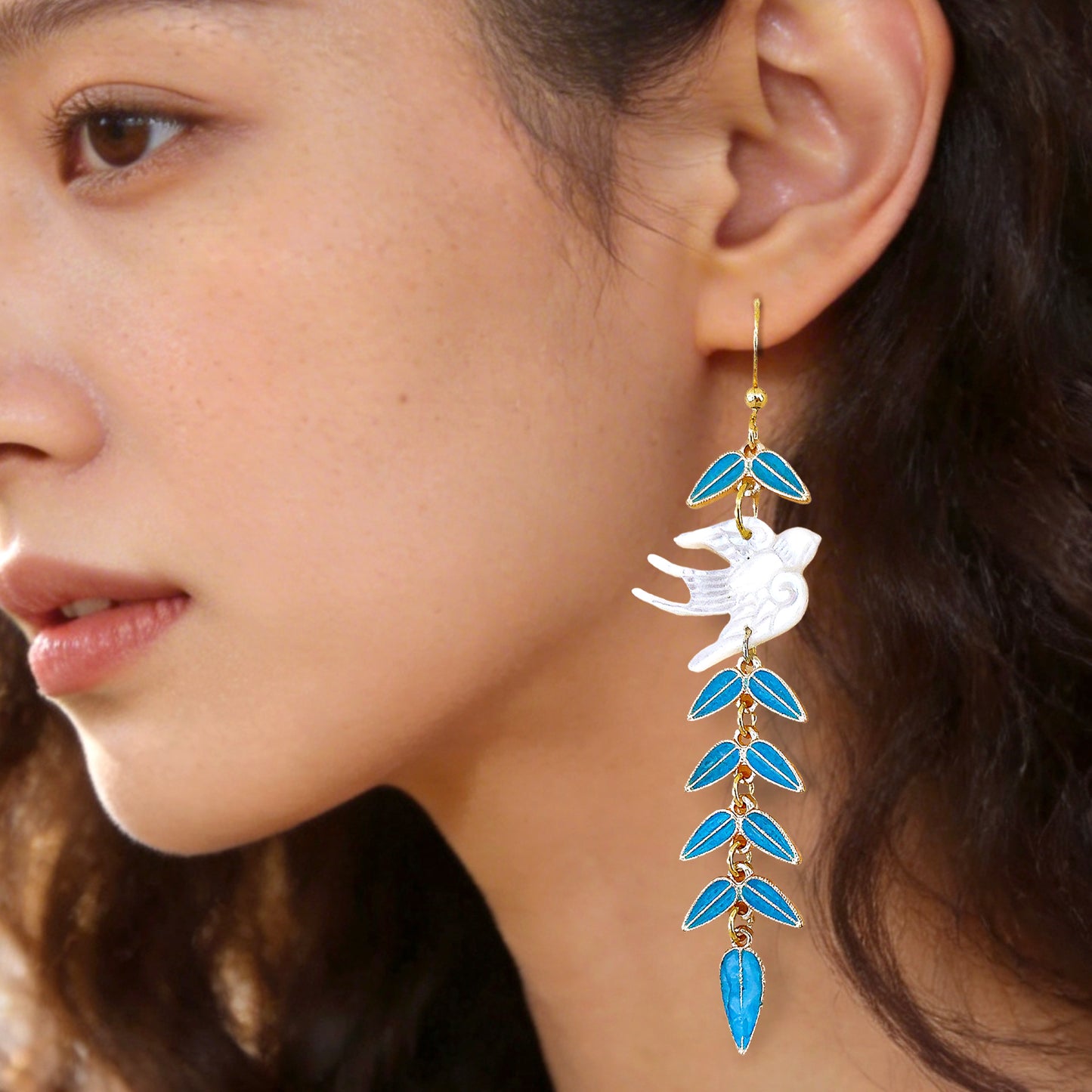 Beautiful young woman wearing unique flying bird and blue vine dangle earrings perfect for a garden party