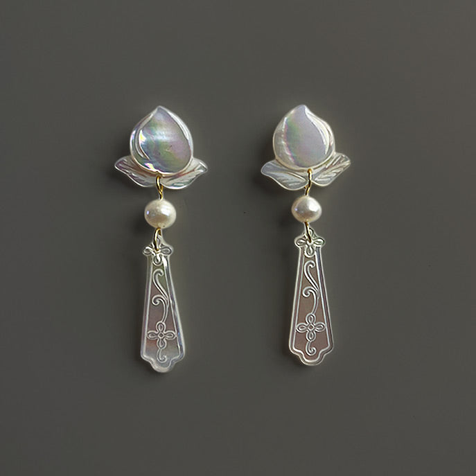 Frontal view of the handmade bridal drop earrings made of deep-sea mother of pearl and delicate freshwater pearls on a grey-brown background.