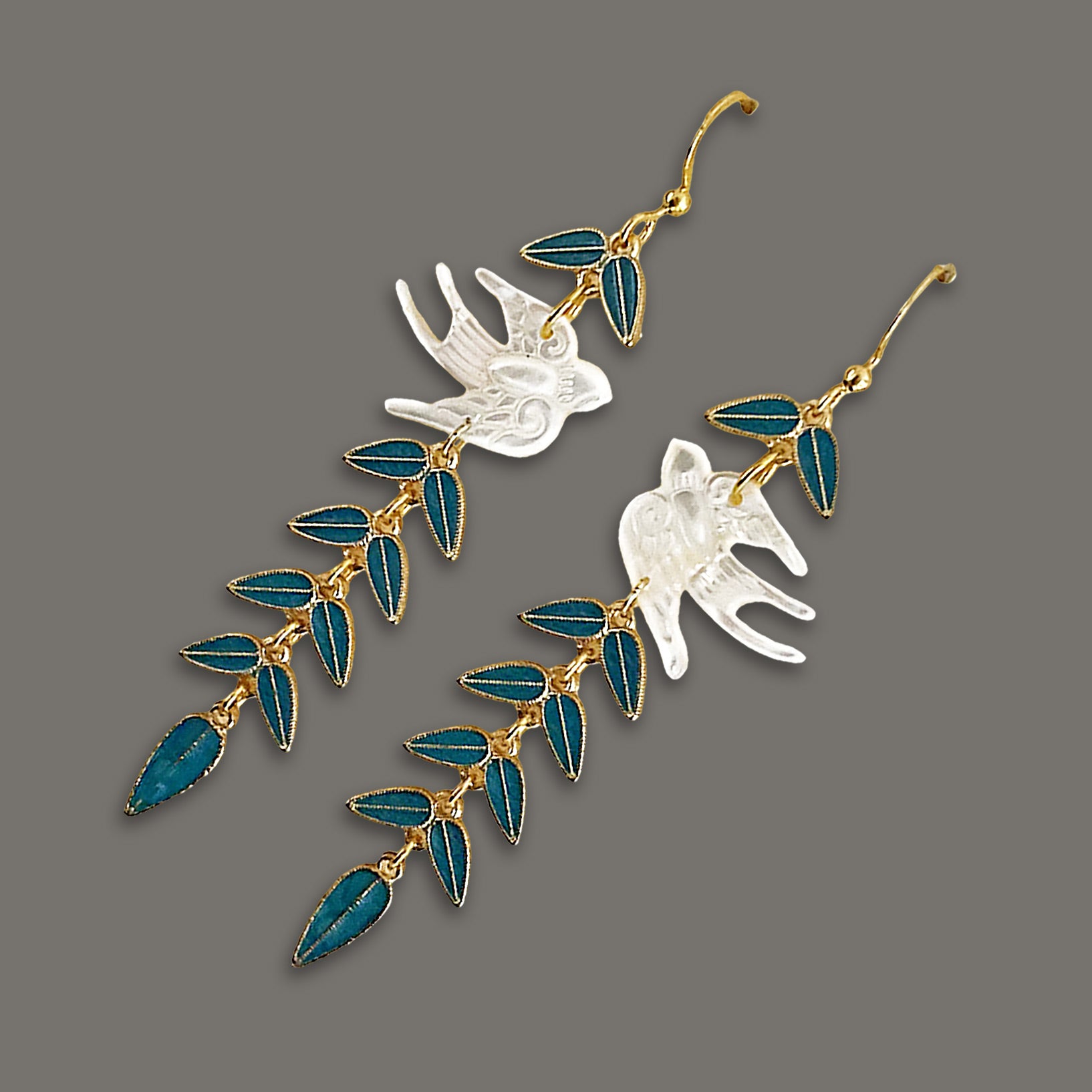Angled view of elegant mother-of-pearl swallow earrings with dangling blue vine leaves on dark background