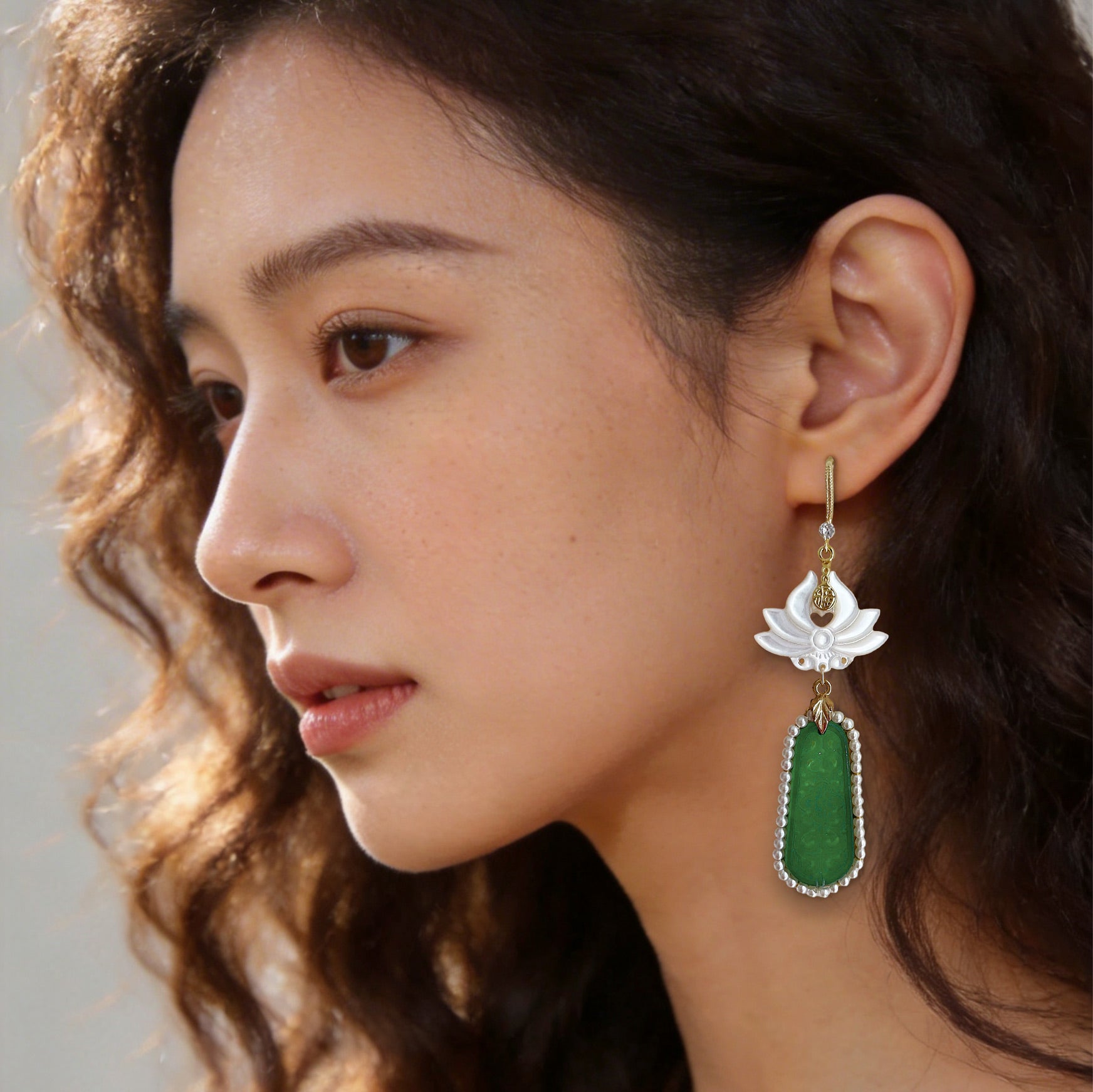 Beautiful woman modeling statement carved shell and emerald green color dangle earrings in warm sunset lighting